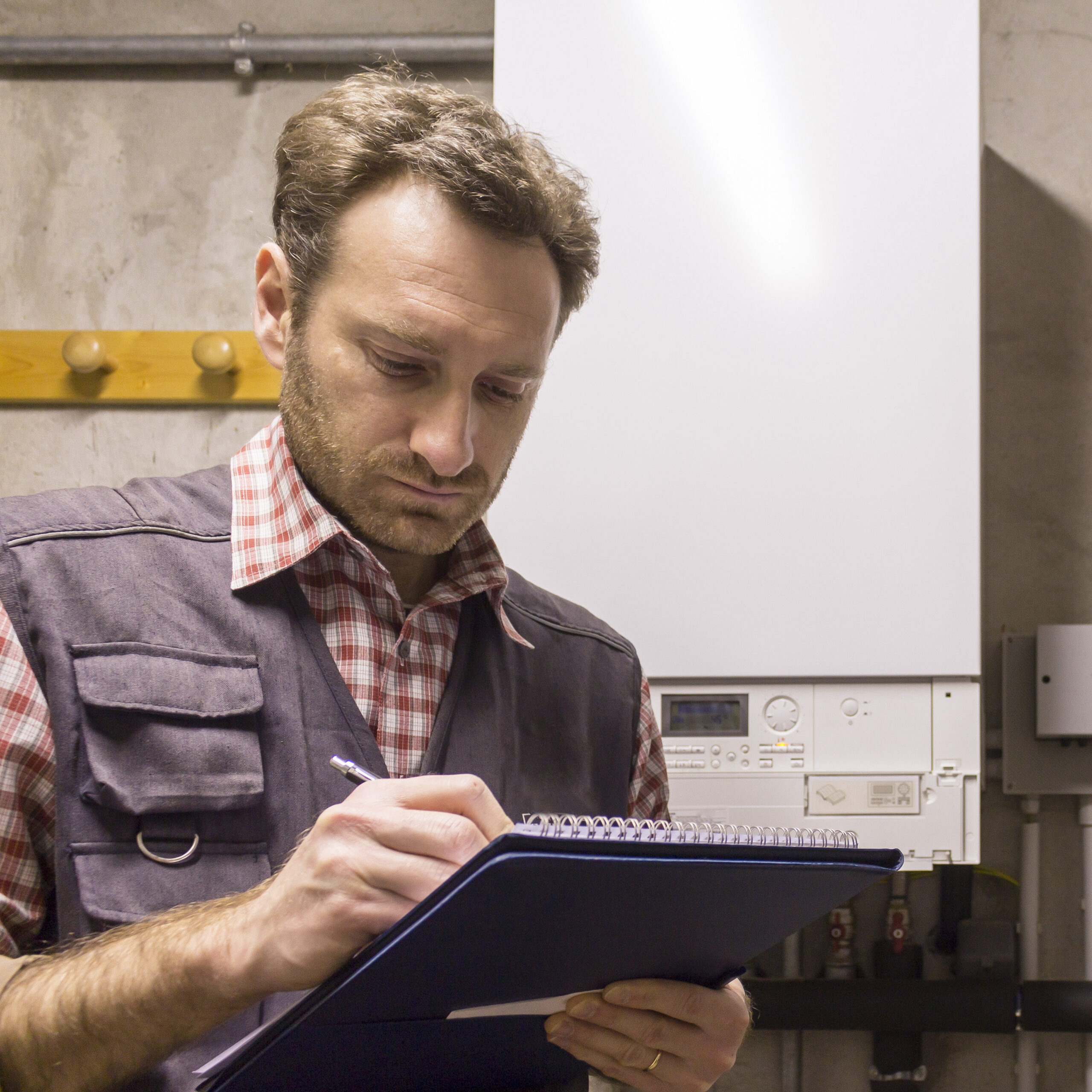 plumber writing clipboard while inspecting heating system scaled